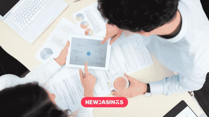 UKGC Deepens Consumer Engagement with New Research Partnerships An overhead shot of two people conferring over a tablet screen showing a plan for business growth alongside papers, alongside a 'NEWCASINOS' logo in pink.