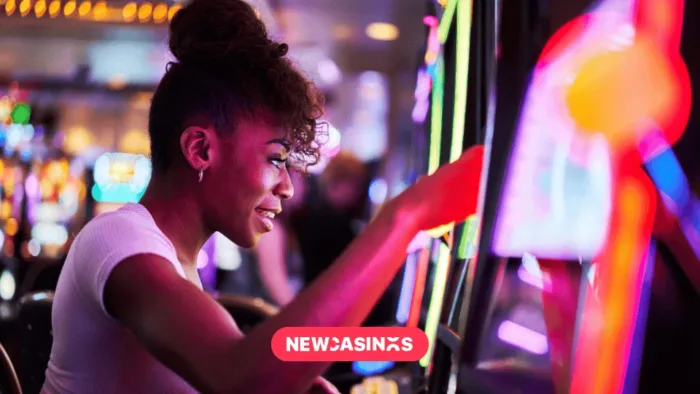 The Hidden Maths Behind Progressive Jackpots and Why It Matters A woman smiling while playing a brightly lit slot machine in a casino, surrounded by colorful lights and gaming machines.