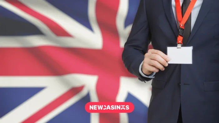 A person with a lanyard on, in front of a Union Jack flag.