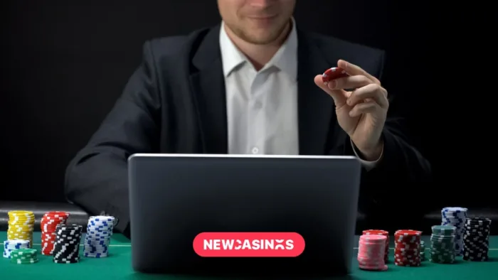 A suited man sitting at laptop holding poker chip.