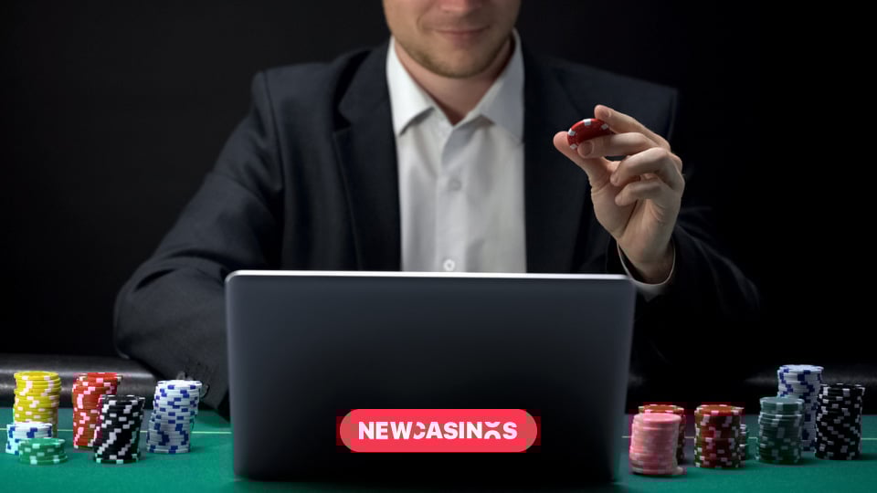A suited man sitting at laptop holding poker chip.