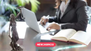 Scales of justice in the foreground of a woman working on a laptop with papers.