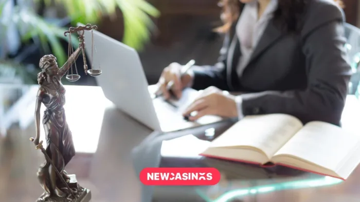 Scales of justice in the foreground of a woman working on a laptop with papers.