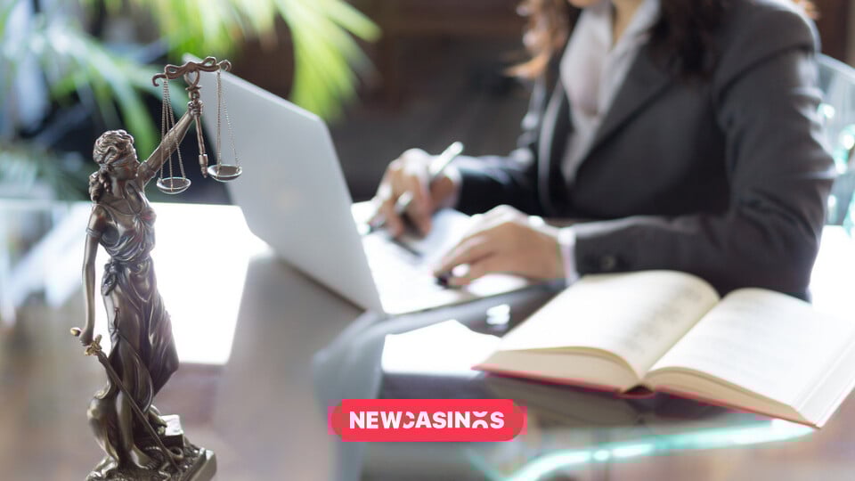 Scales of justice in the foreground of a woman working on a laptop with papers.