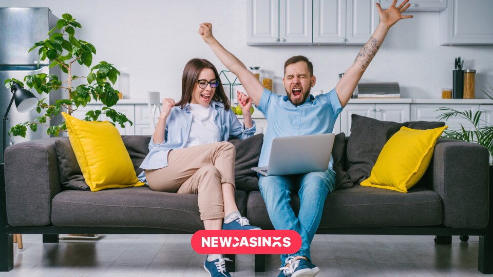 A couple sitting on their couch celebrating with an open laptop.